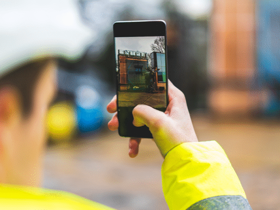Mann mit Warnjacke macht mit einem Smartphone eine Bild von einem Gebäude